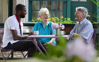 seniors en maison de repos déjeunant en terrasse avec un infirmier